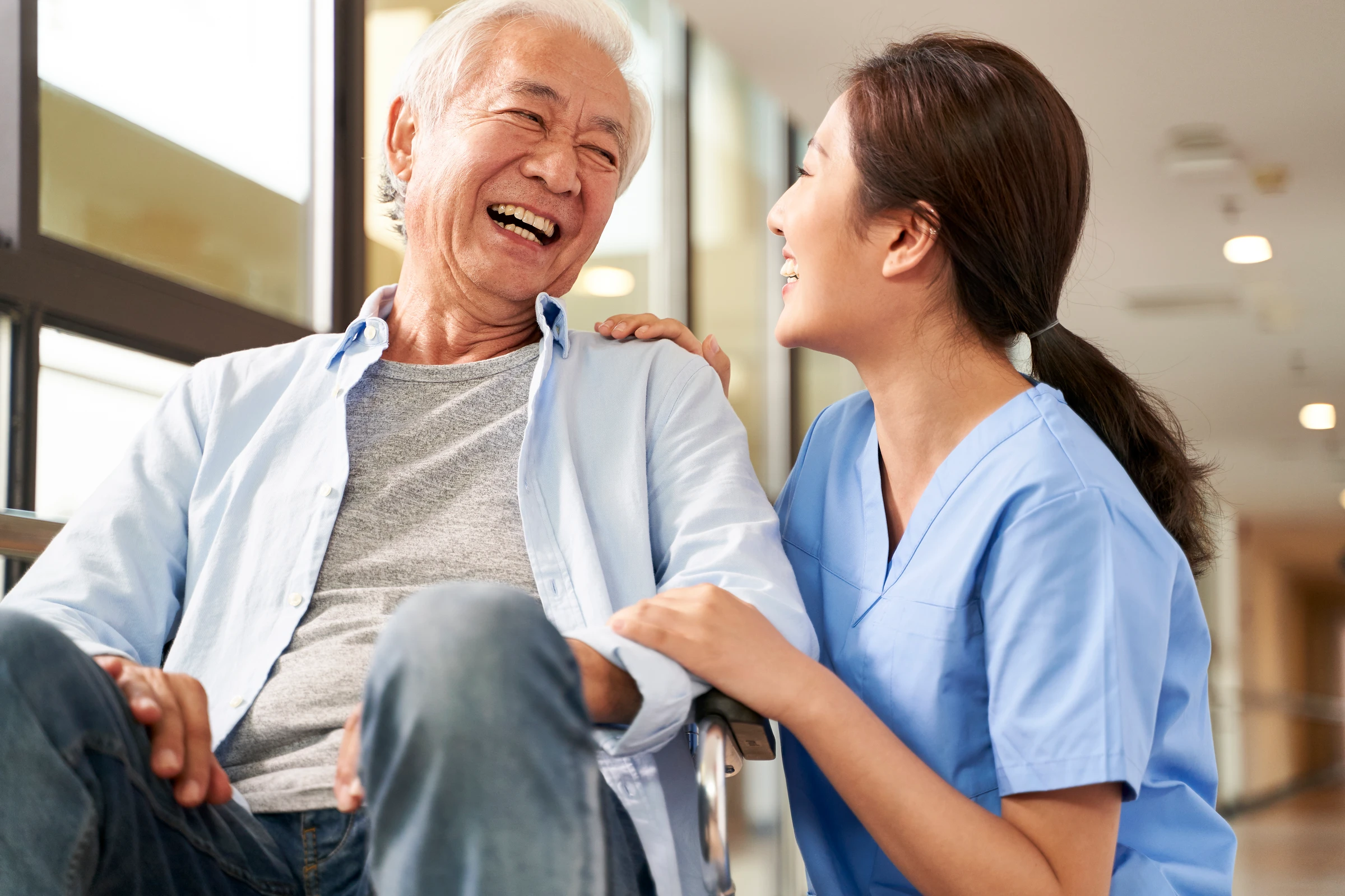 A smiling Asian nurse sharing a warm, friendly moment with a laughing older Asian patient